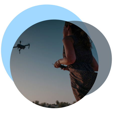 A woman operating a drone in mid-air at sunset.